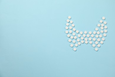 Photo of Endocrinology, Shape of thyroid gland made of pills on light blue background, flat lay. Space for text