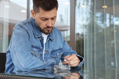 Man holding cigarette over glass ashtray at table outdoors