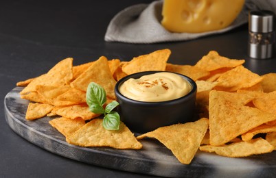 Delicious nachos and cheese sauce with basil on black table