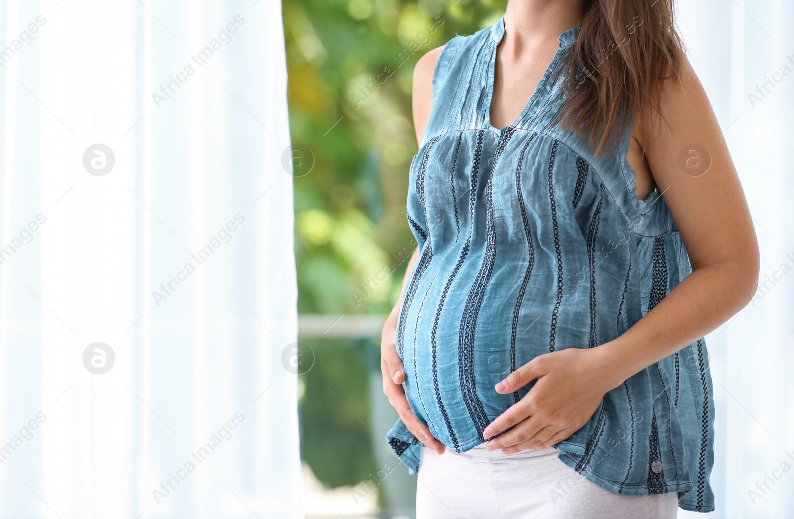 Photo of Pregnant woman standing near window at home, closeup