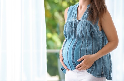 Photo of Pregnant woman standing near window at home, closeup