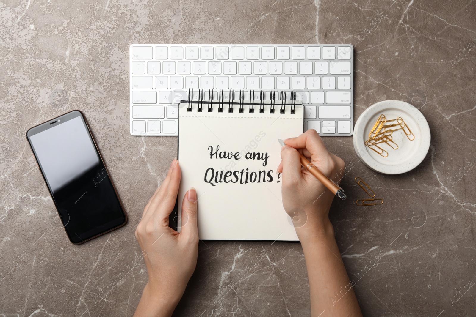 Photo of Woman writing phrase HAVE ANY QUESTIONS in notebook at grey marble table, top view