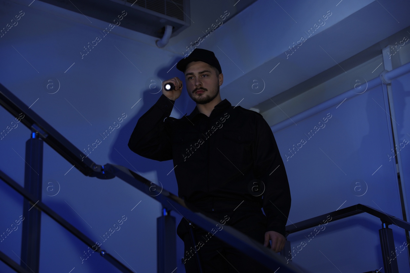 Photo of Male security guard with flashlight on stairs in darkness