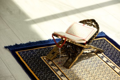 Photo of Rehal with open Quran and Misbaha on Muslim prayer rug indoors, space for text