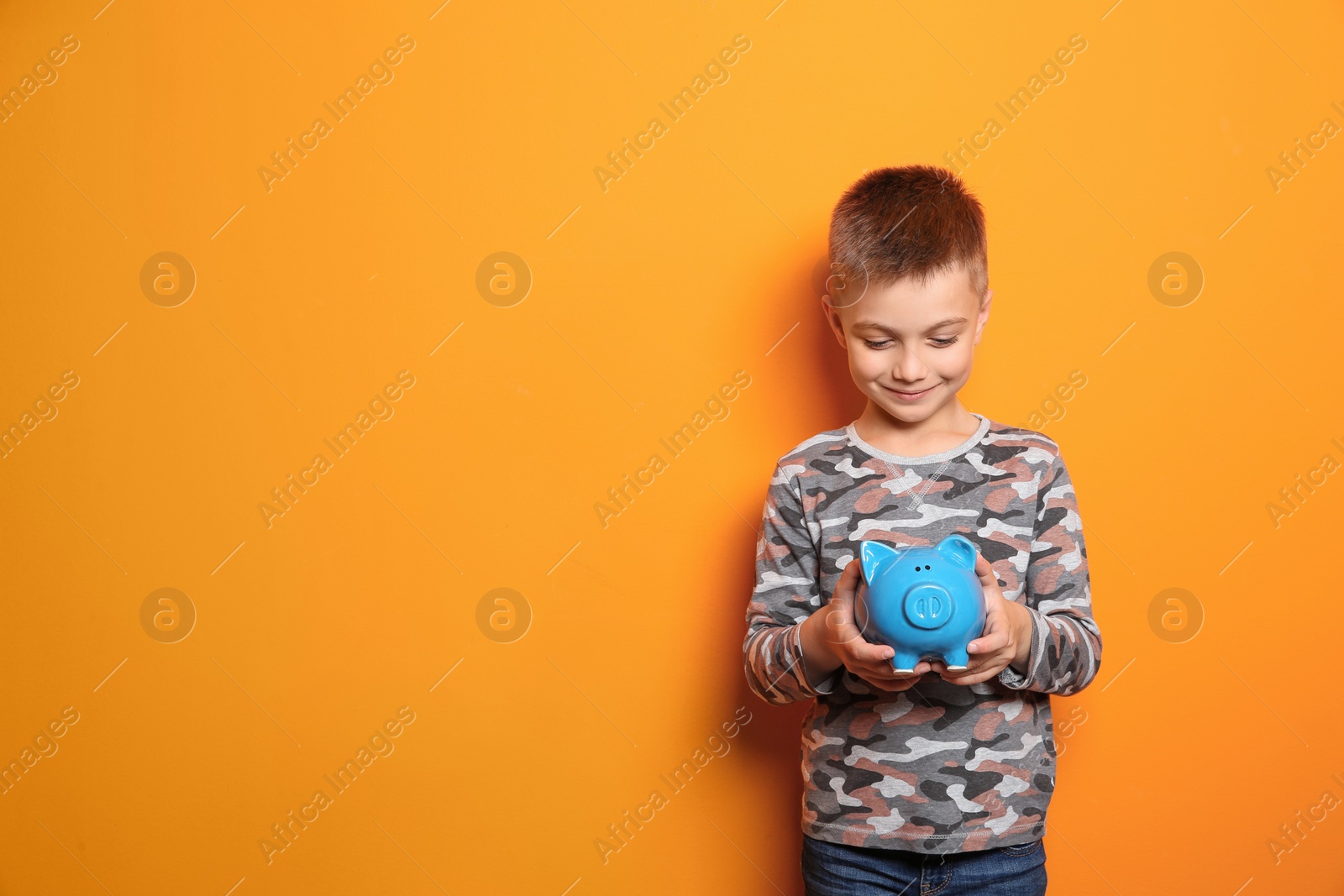 Photo of Little boy with piggy bank on color background. Space for text