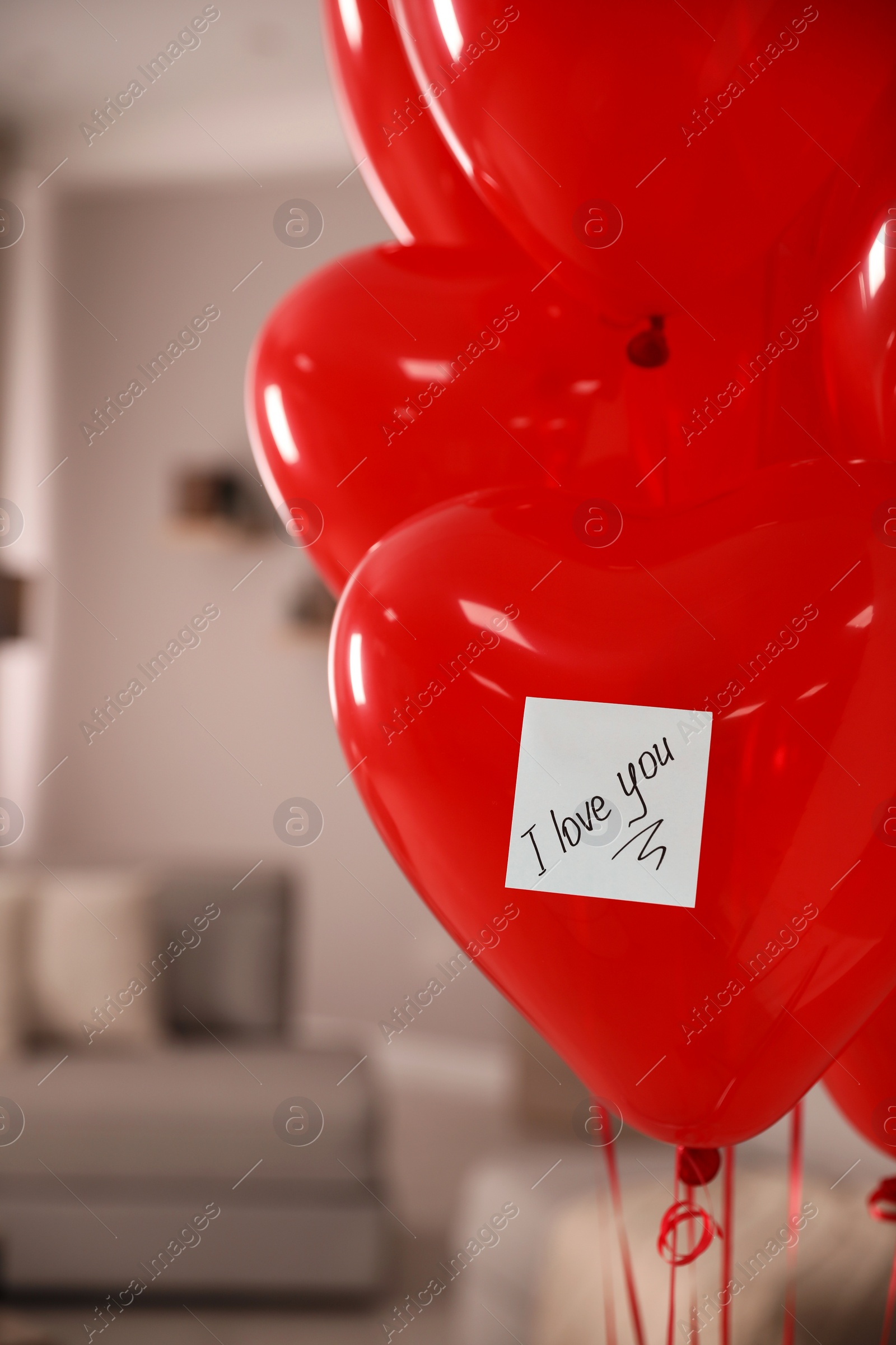 Photo of Red heart shaped air balloons with sticky note saying I Love You in room