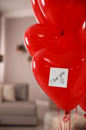 Red heart shaped air balloons with sticky note saying I Love You in room