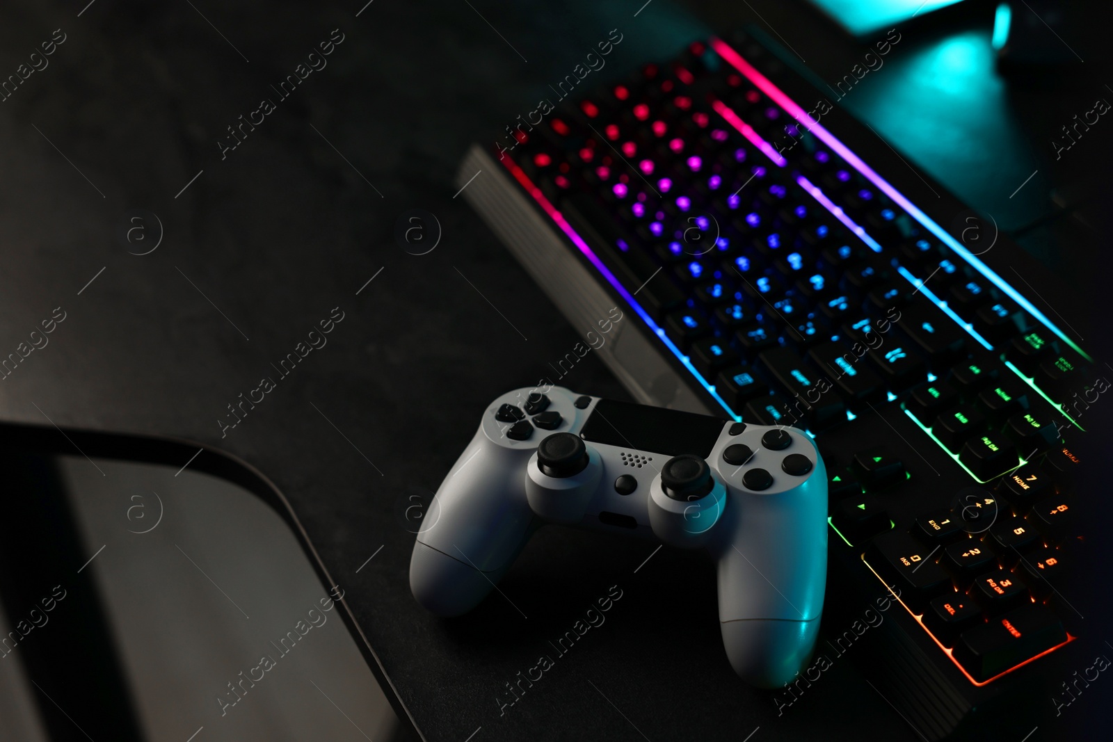 Photo of Playing video games. Computer keyboard with RGB lighting and wireless controller on table indoors