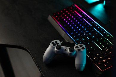 Photo of Playing video games. Computer keyboard with RGB lighting and wireless controller on table indoors