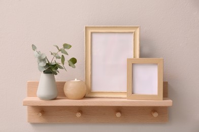 Photo of Wooden shelf with photo frames, candle and eucalyptus on beige wall. Interior element