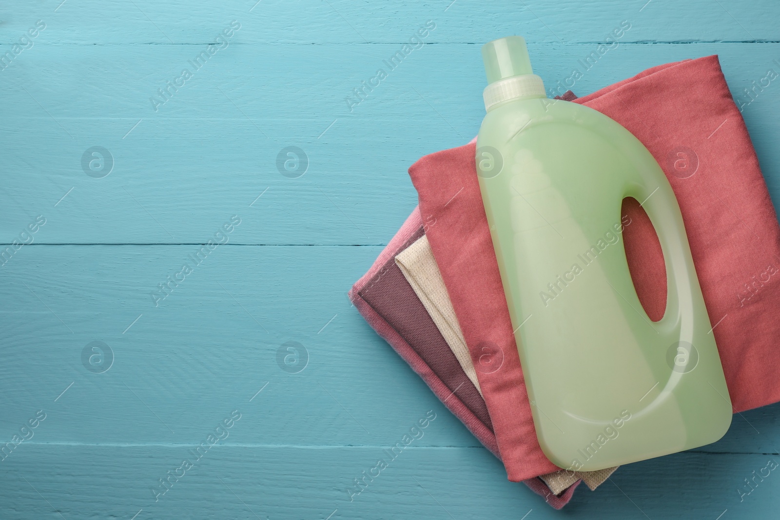 Bottle of fabric softener and stacked clean clothes on light blue wooden table, top view. Space for text Photo of Bottle of fabric softener and stacked clean clothes on light blue wooden table, top view. Space for text