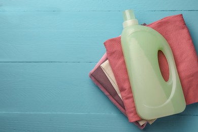 Photo of Bottle of fabric softener and stacked clean clothes on light blue wooden table, top view. Space for text