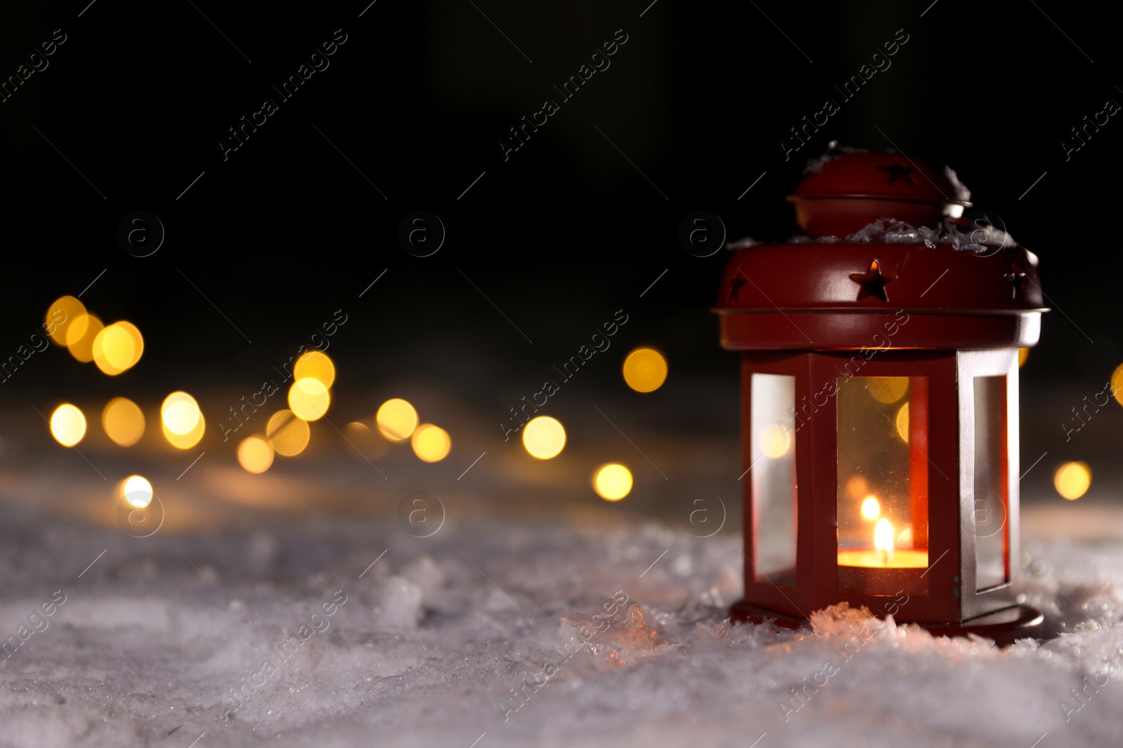 Photo of Lantern with burning candle and Christmas lights on white snow outdoors. Space for text