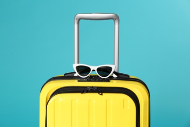 Photo of Stylish suitcase with sunglasses on color background