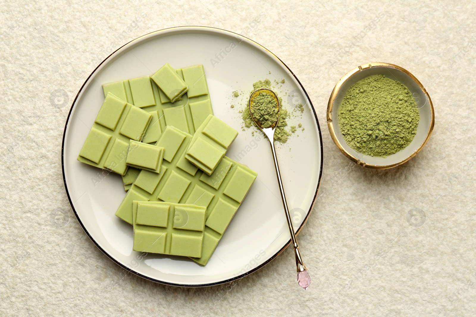 Photo of Pieces of tasty matcha chocolate bar and powder in spoon on white textured table, top view