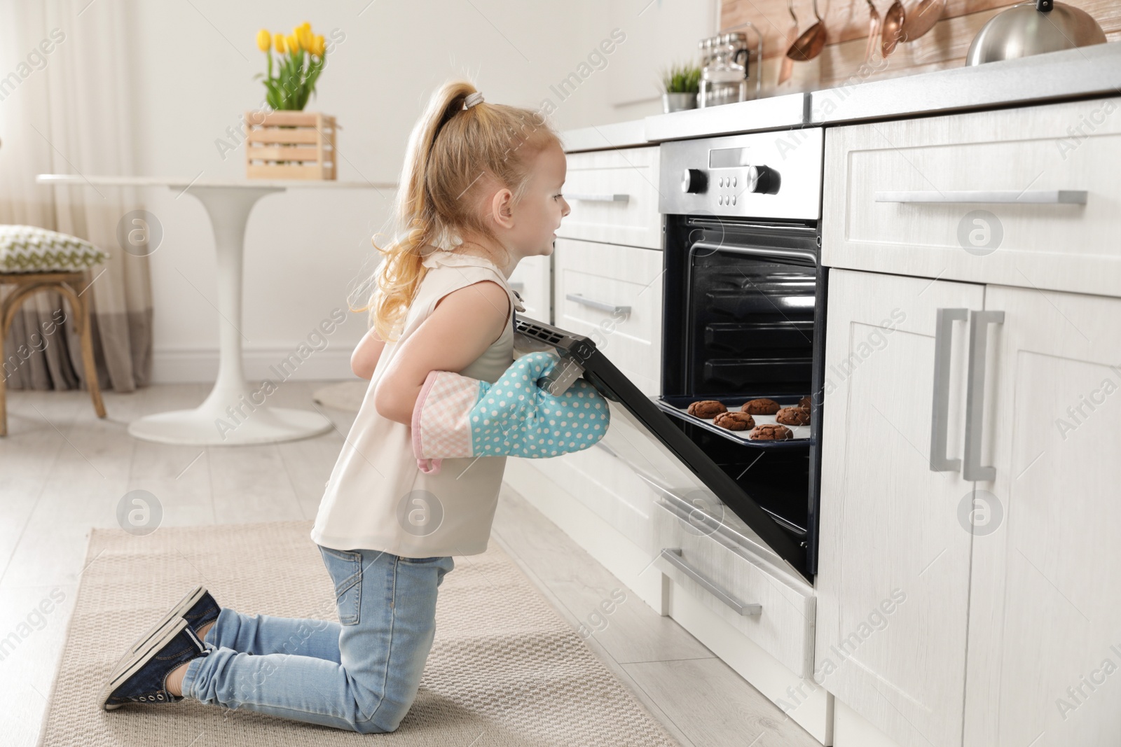 Photo of Little girl opening door of oven with cookies in kitchen