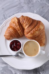 Photo of Tasty breakfast. Cup of coffee, fresh croissants and jam on grey table, top view