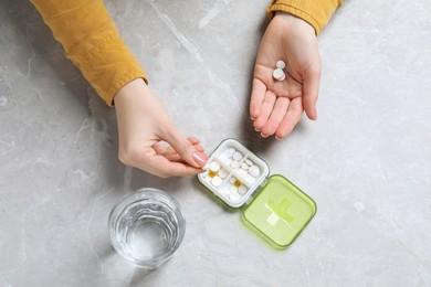 Photo of Woman putting pill into plastic box at grey marble table, top view