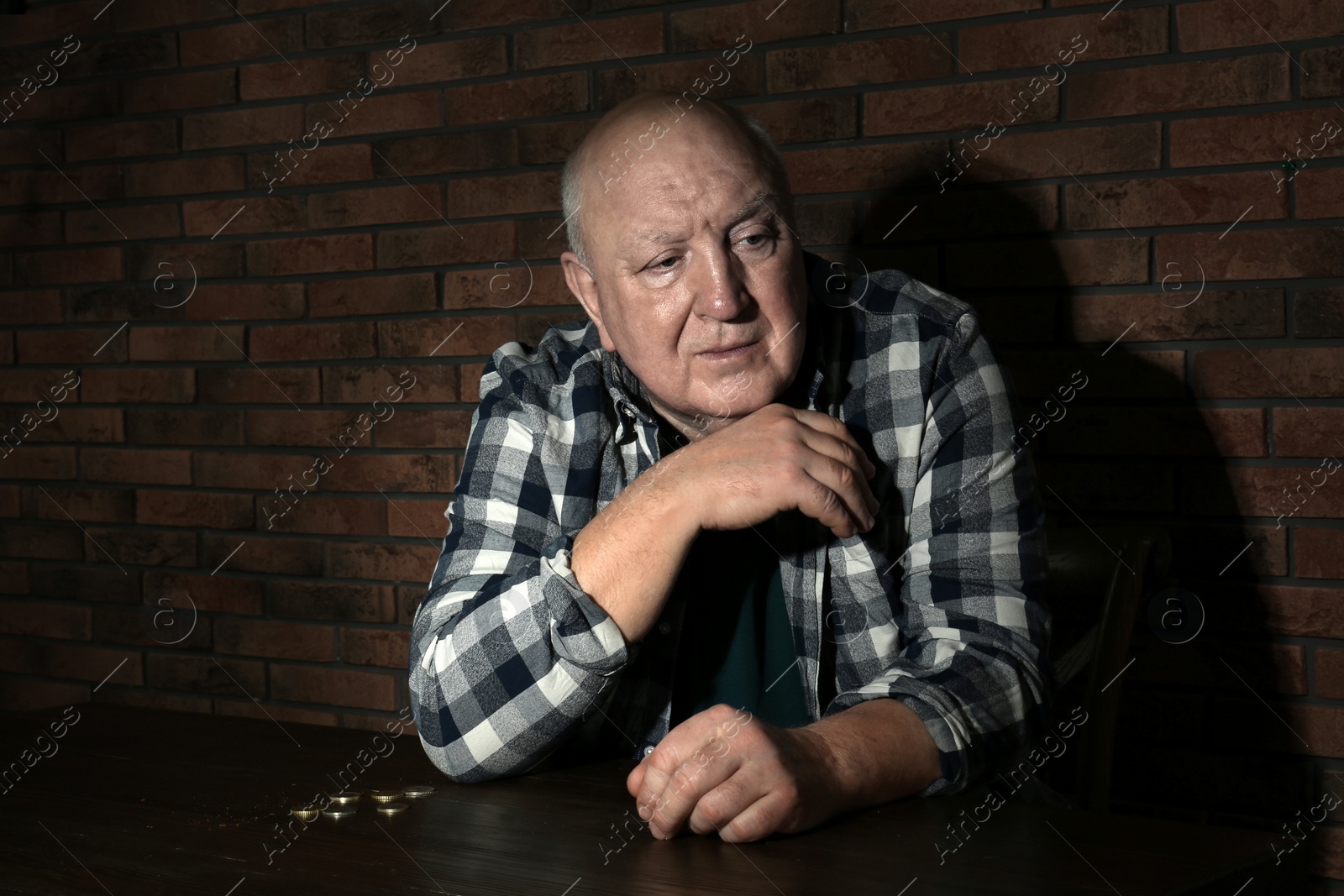 Photo of Poor senior man with coins at table near brick wall