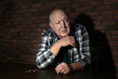 Poor senior man with coins at table near brick wall