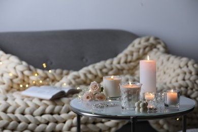 Photo of Burning candles, flowers and jewelry on table in room