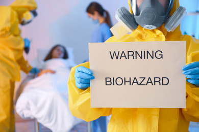 Paramedic holding sign with words WARNING BIOHAZARD in quarantine ward, closeup. Virus awareness