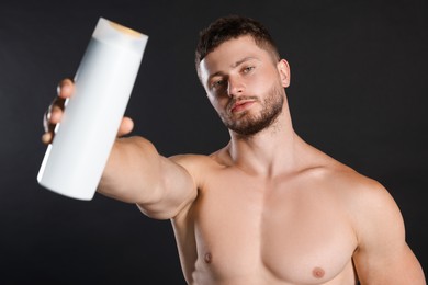 Shirtless young man holding bottle of shampoo on black background
