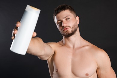 Photo of Shirtless young man holding bottle of shampoo on black background