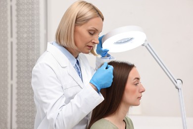 Photo of Trichologist examining patient`s hair under lamp in clinic