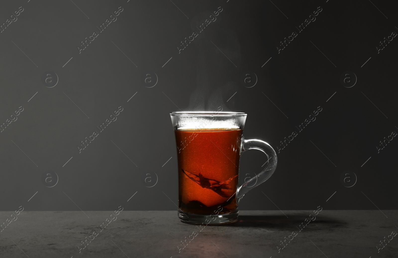 Photo of Glass cup of hot leaf tea on stone table against grey background, space for text