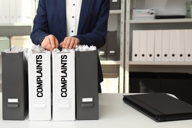 Woman searching through documents in folder with Complaints label in office, closeup