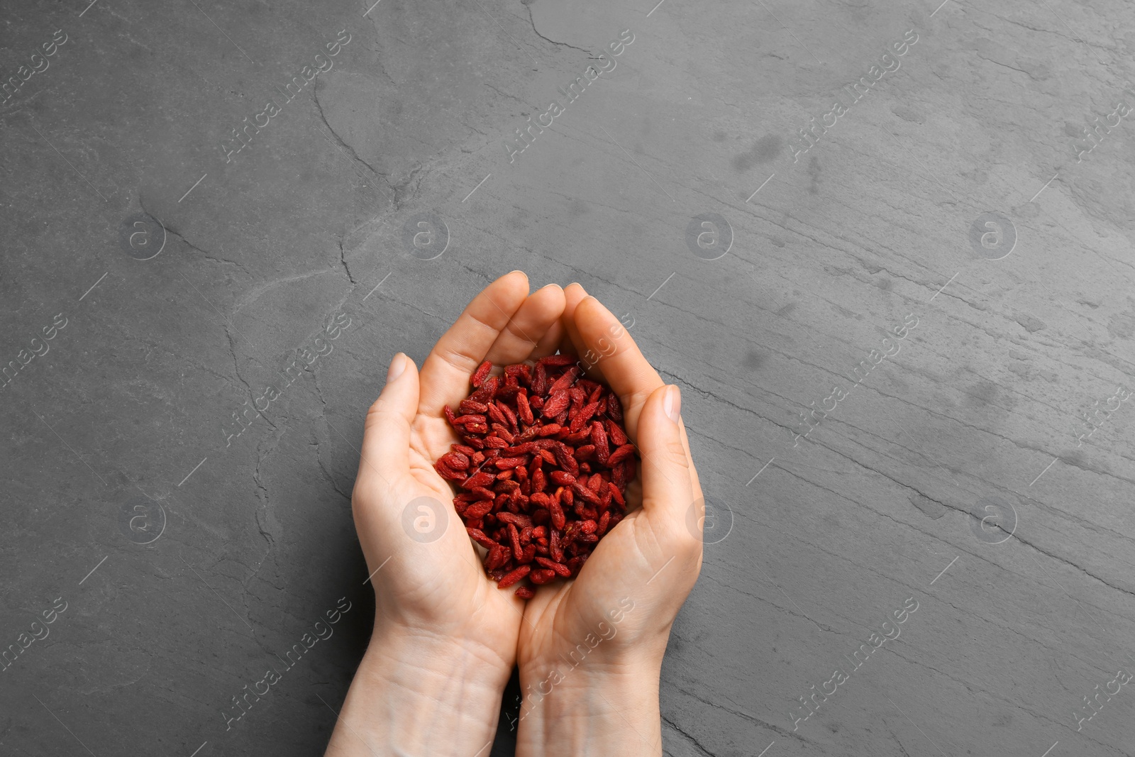 Photo of Woman holding red dried goji berries on grey stone background, top view