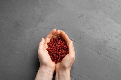 Woman holding red dried goji berries on grey stone background, top view
