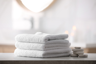Photo of Stack of fresh towels and spa stones on table in bathroom