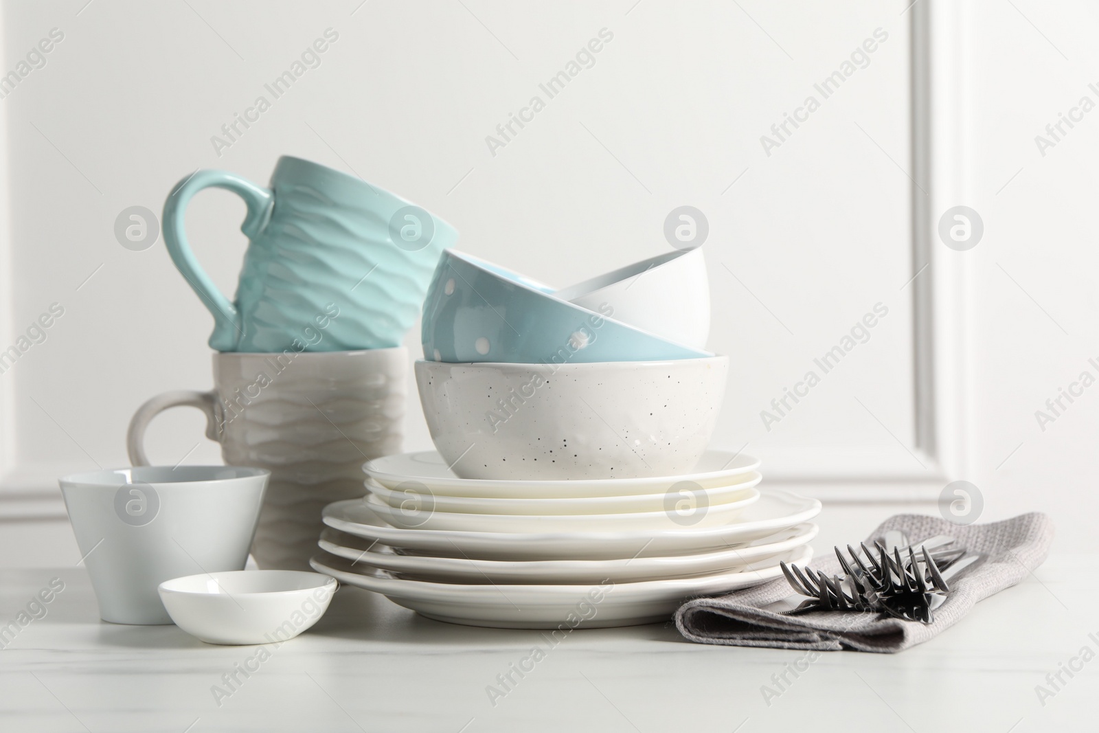 Photo of Beautiful ceramic dishware, cups and cutlery on white marble table