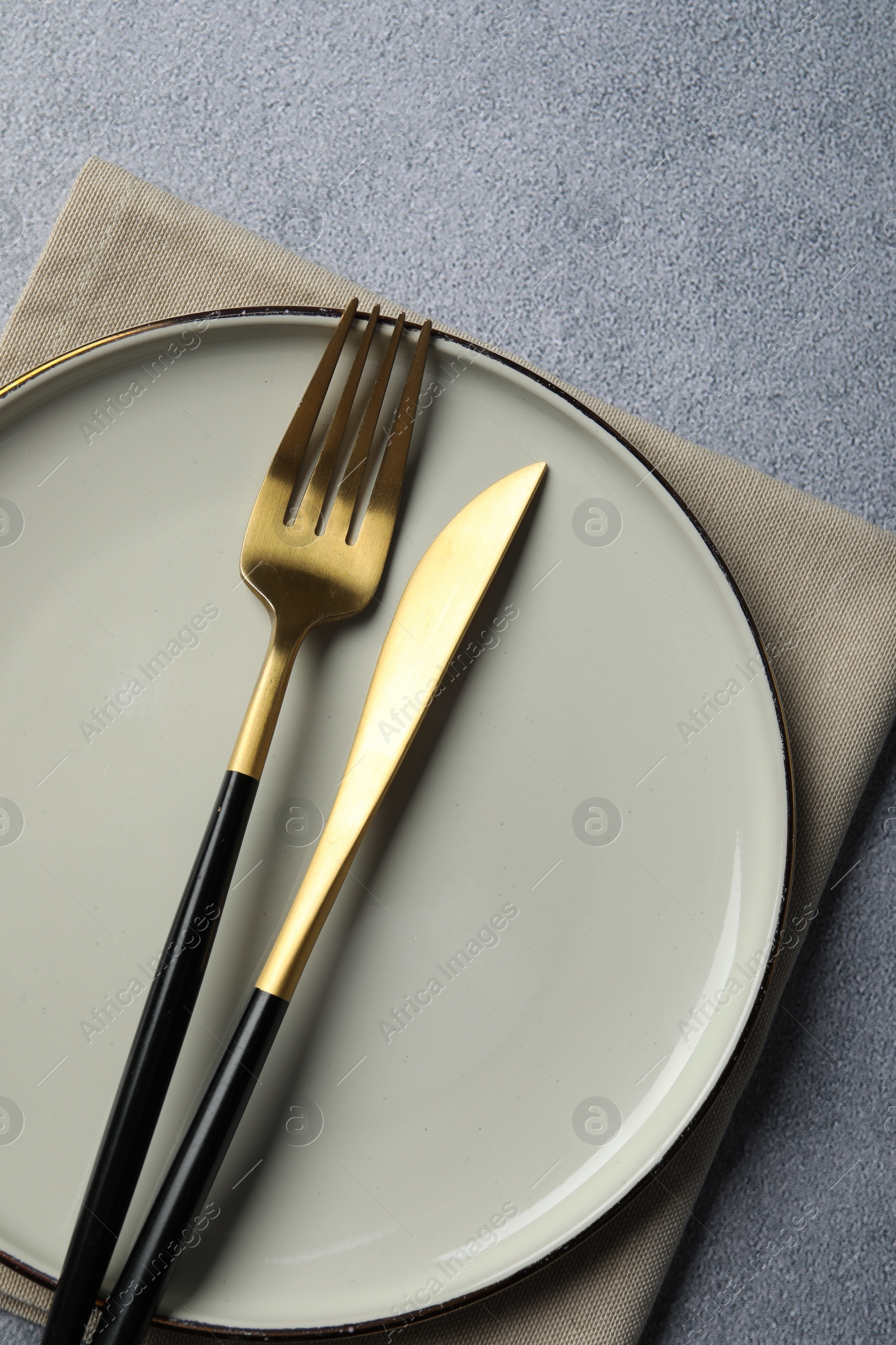 Photo of Stylish golden cutlery, plate and napkin on grey table, top view