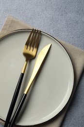 Photo of Stylish golden cutlery, plate and napkin on grey table, top view