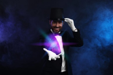 Image of Magic and sorcery. Magician with fantastic light in smoke on dark background