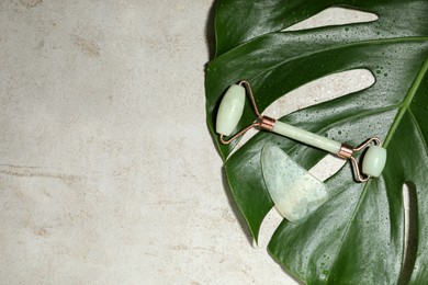 Photo of Gua sha stone, face roller and monstera leaf on light table, flat lay. Space for text