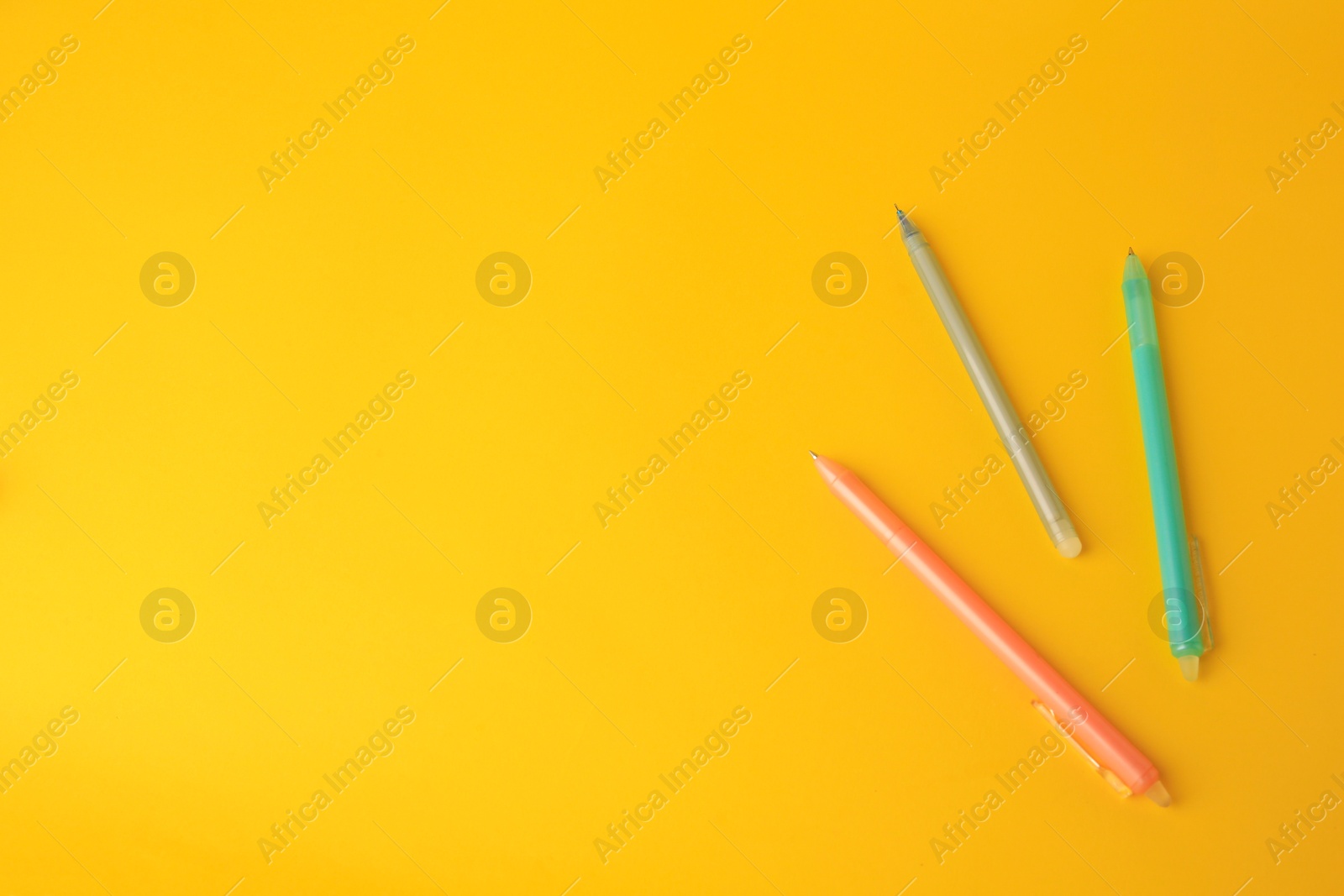 Photo of Three erasable pens on yellow background, flat lay. Space for text