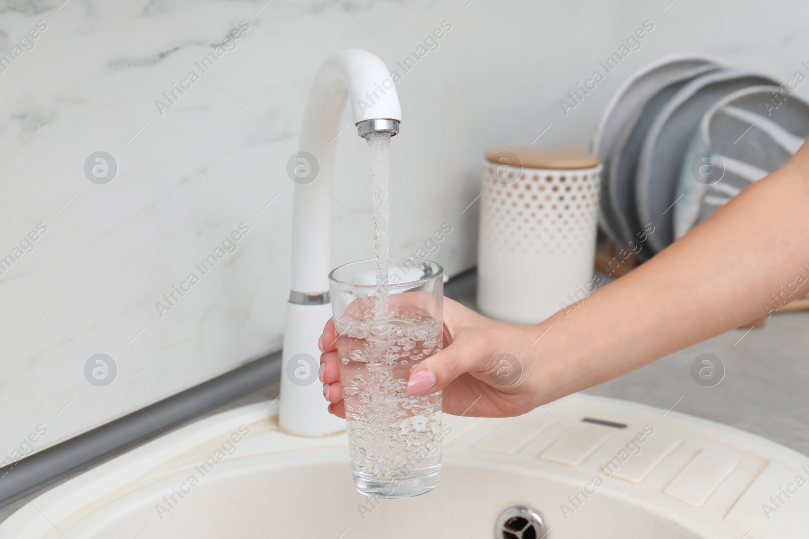 Photo of Woman filling glass with water from faucet in kitchen, closeup