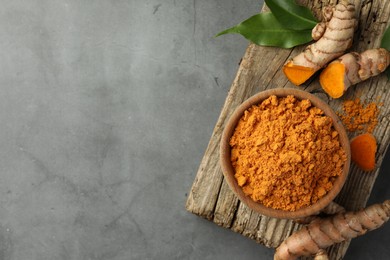 Photo of Aromatic turmeric powder and raw roots on grey table, top view. Space for text