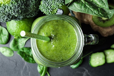 Photo of Delicious green juice and fresh ingredients on black table, flat lay