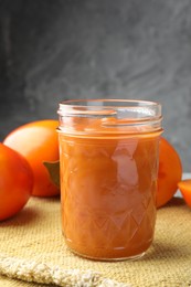 Photo of Delicious persimmon jam in glass jar and fresh fruits on table