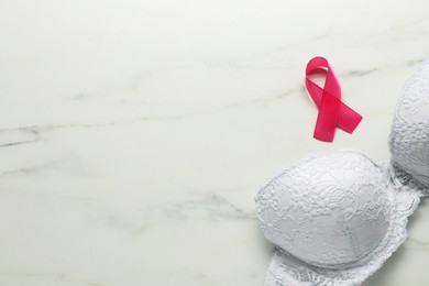 Photo of Breast cancer awareness. Pink ribbon and bra on white marble table, flat lay. Space for text