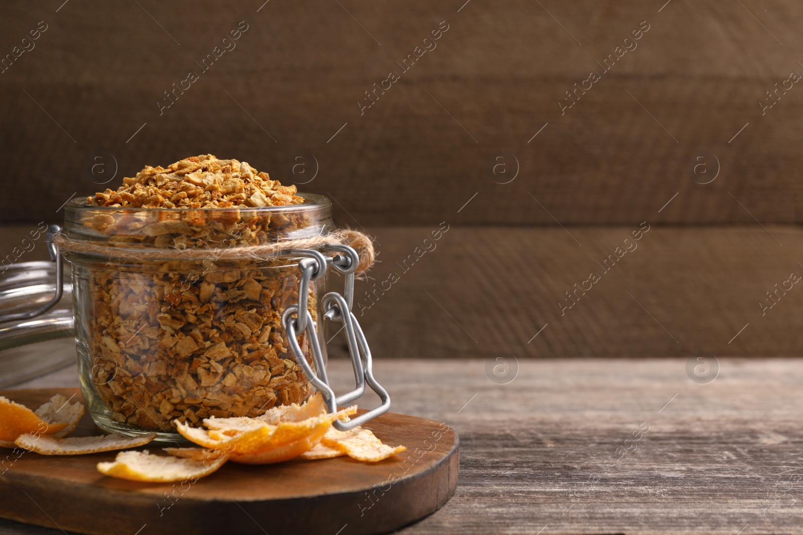 Photo of Jar of dried orange zest seasoning and fresh peel on wooden table. Space for text