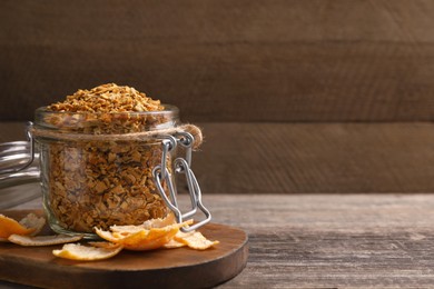 Photo of Jar of dried orange zest seasoning and fresh peel on wooden table. Space for text