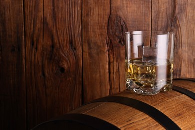 Whiskey with ice cubes in glass on barrel against wooden background, space for text