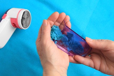 Photo of Woman emptying fabric shaver above light blue cloth, closeup