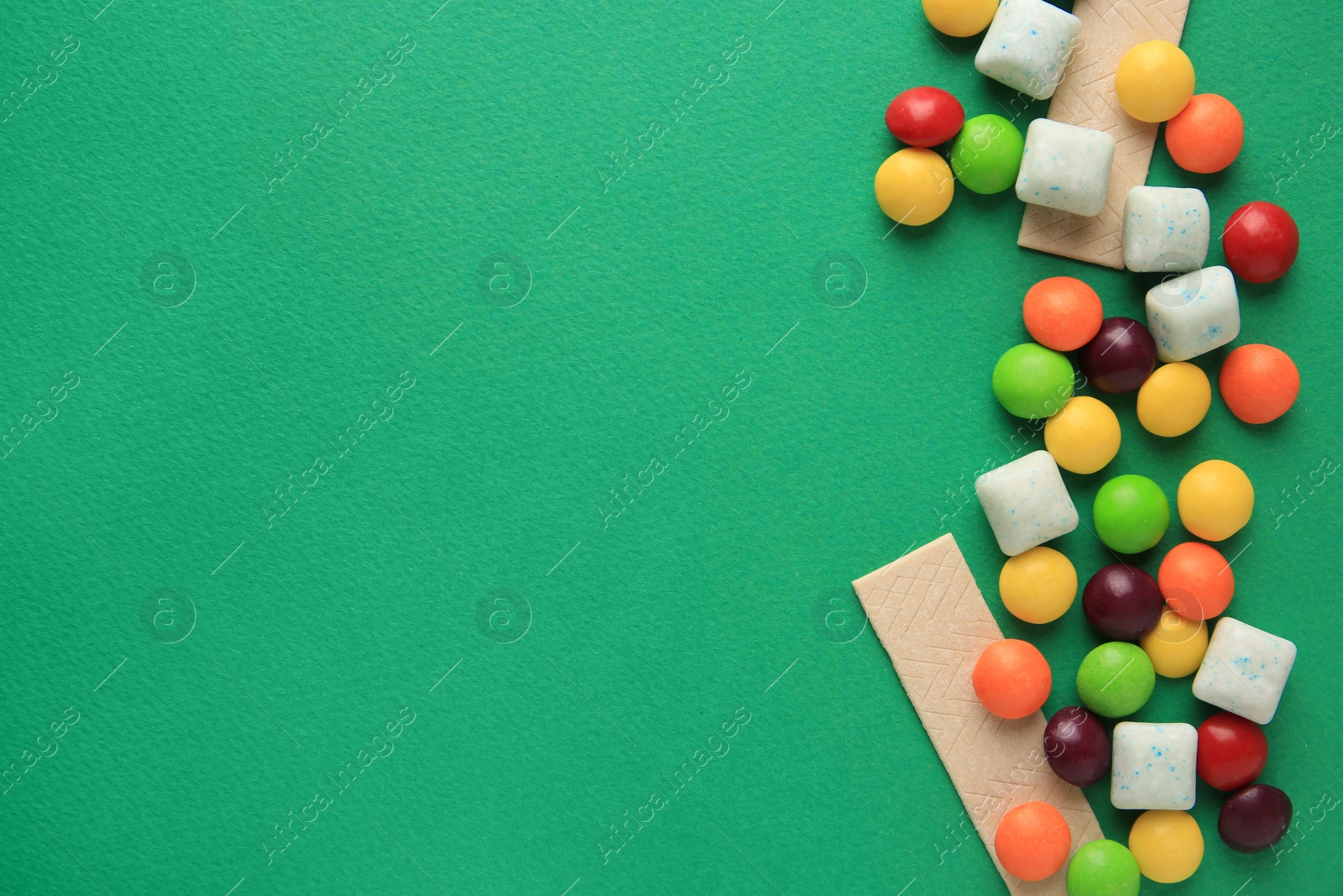 Photo of Different tasty chewing gums on green background, flat lay. Space for text